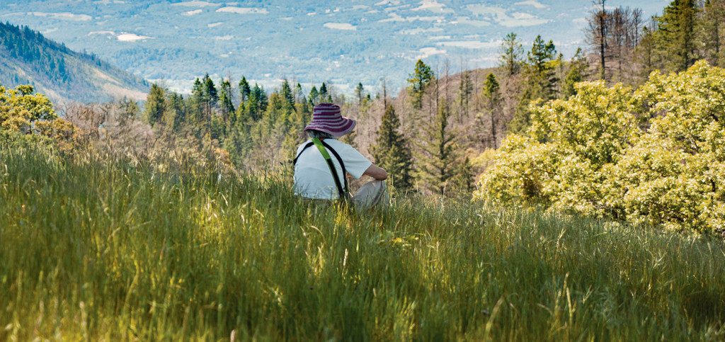 A hiker stops to sit in a meadow and take in the views from Hood Mountain