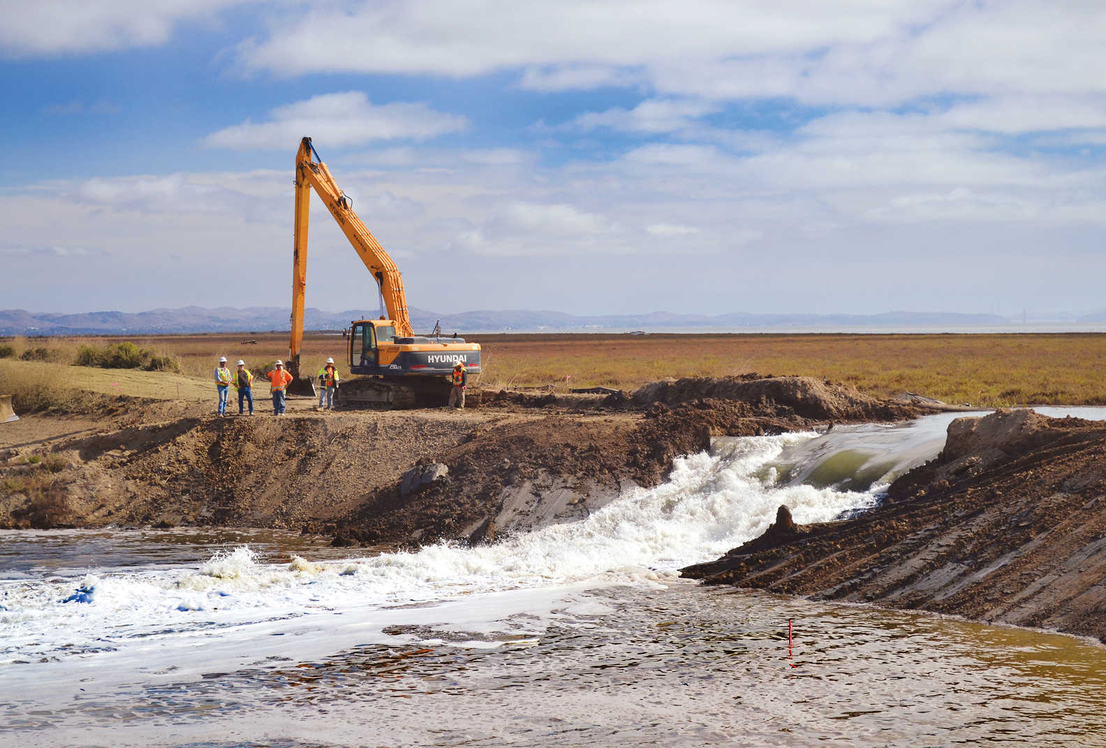 A piece of heavy machinery with several workers next to it performing a levee breach at Sears Point Ranch.