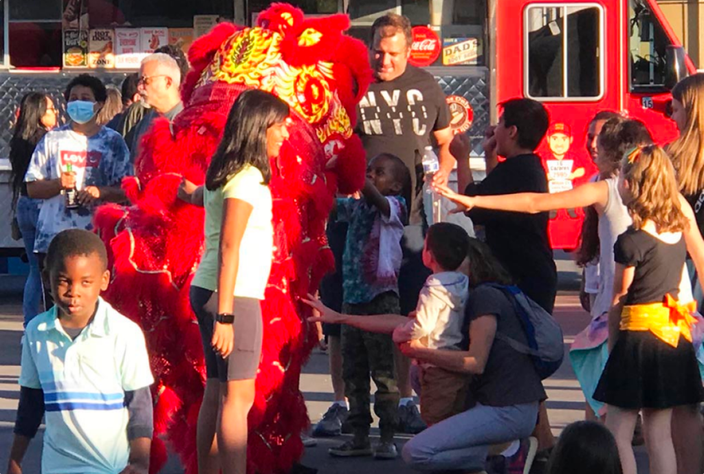 Chinese dragon puppet with event attendees and fire truck in background.