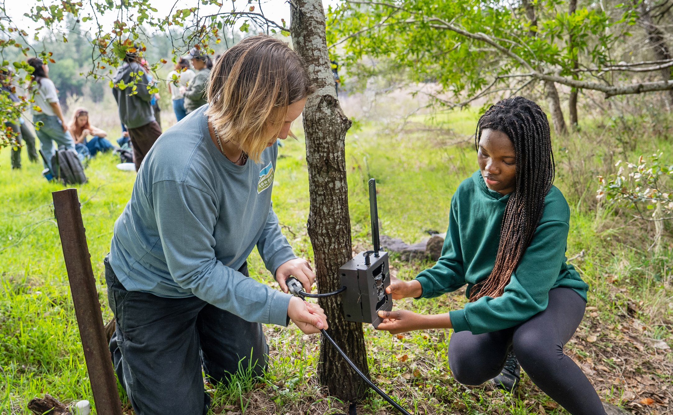 Conservation Council members attach a wildlife camera to a tree.