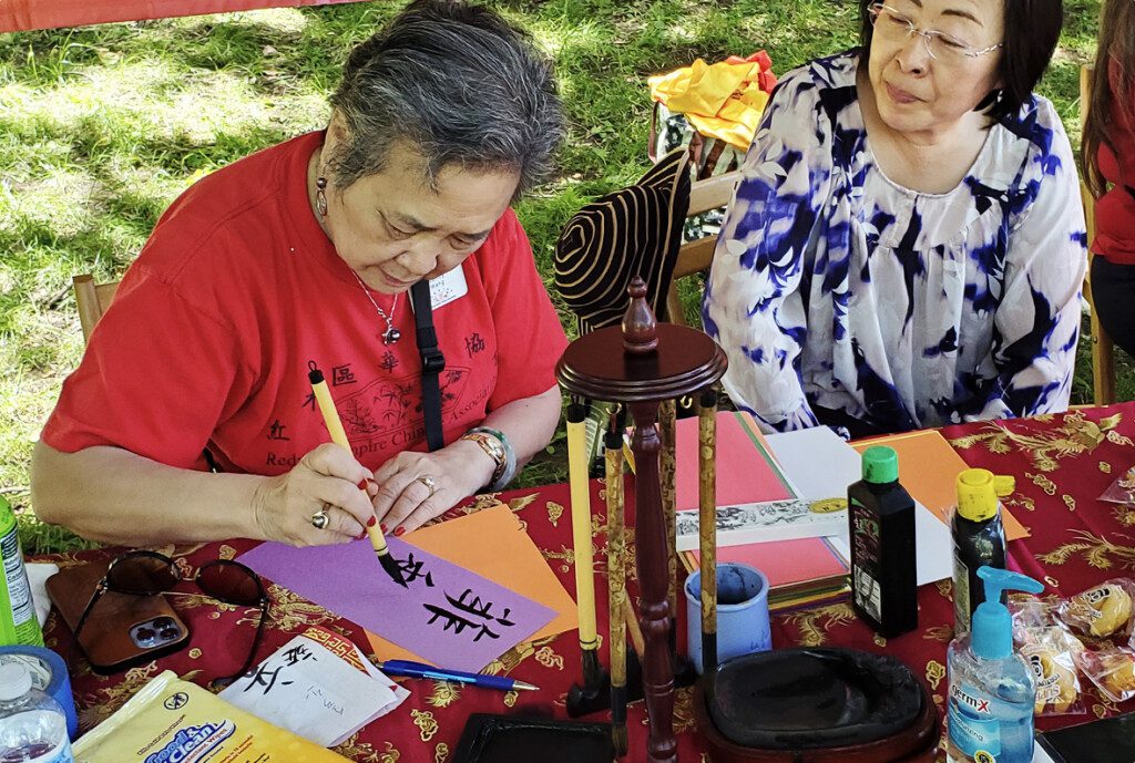 Two people writing Chinese characters in ink with brush.